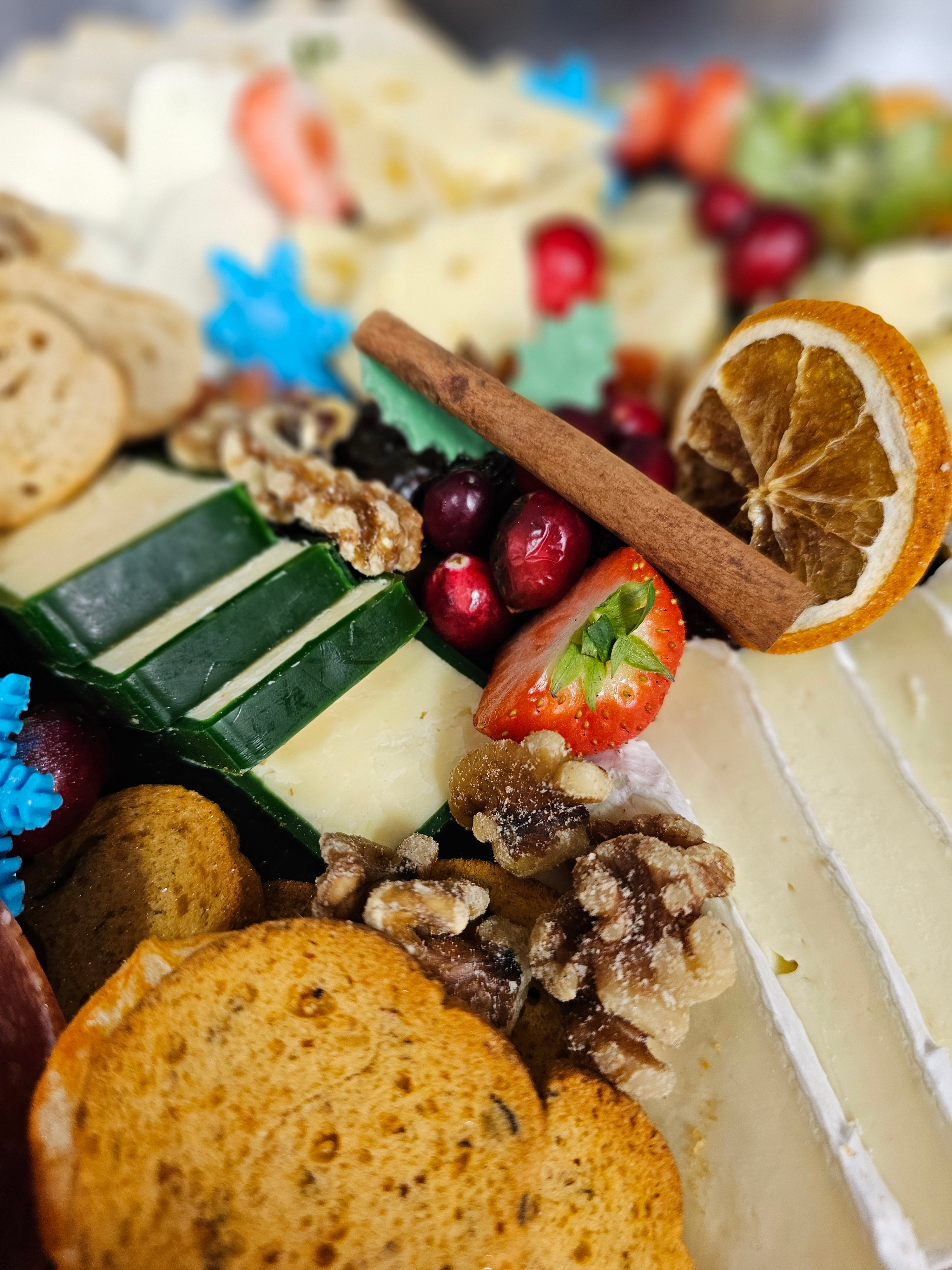 Close-up of a festive cheese board from Cake Secret's Christmas afternoon tea, featuring assorted cheeses, crackers, walnuts, cranberries, strawberries, dried orange slices, and a cinnamon stick, decorated with holiday accents.